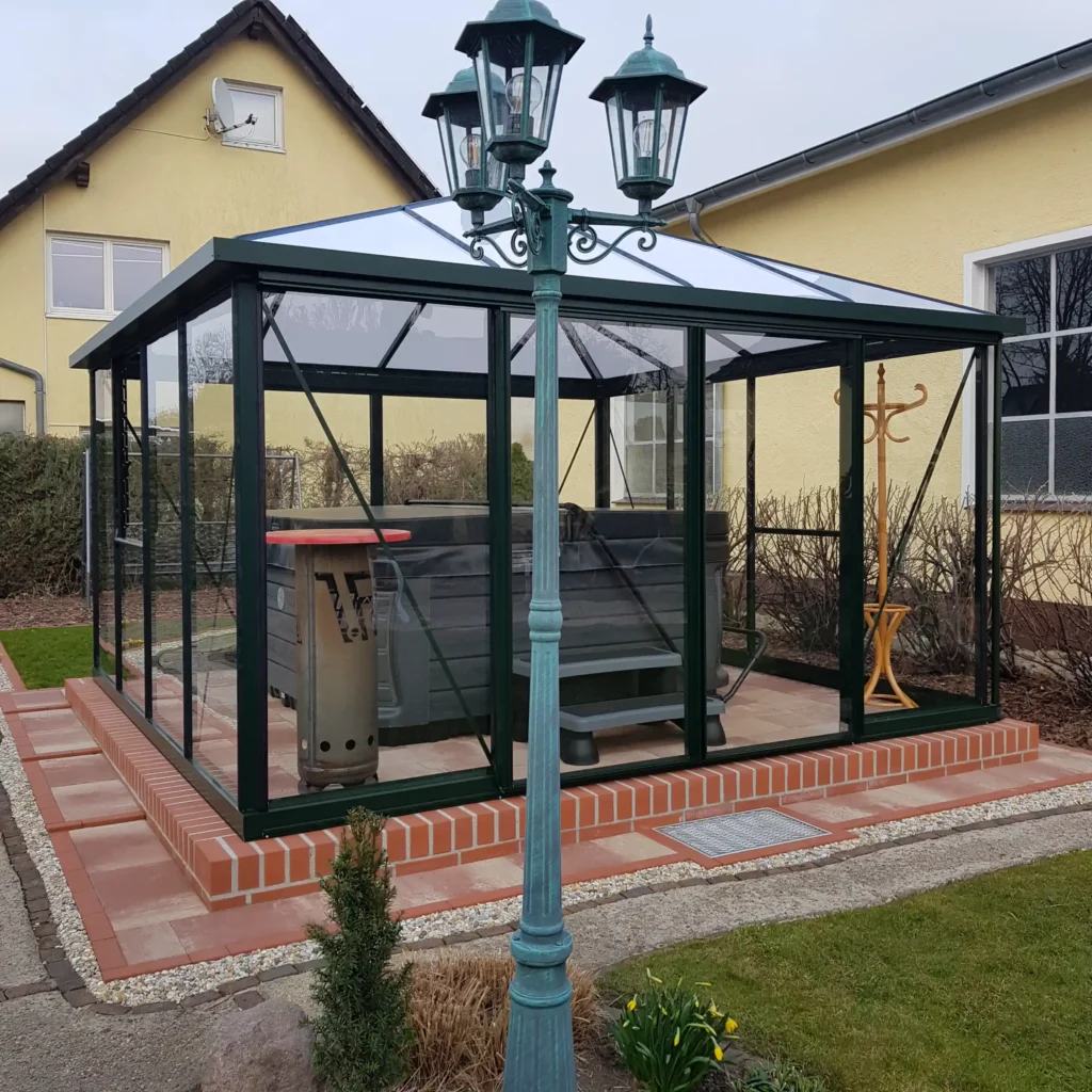 Gartenpavillon aus Glas mit Sitzmöbeln, Laternenmast im Vordergrund. HOGATEK von Hof und Garten Wittstock.